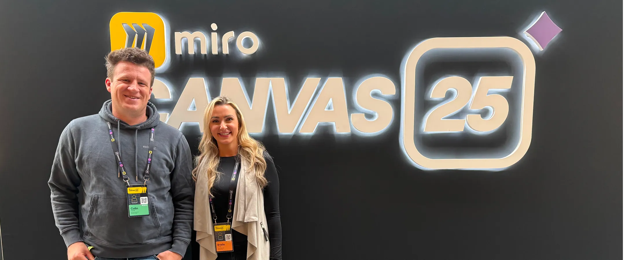 Two colleagues standing in front of the Miro Canvas 25 signage