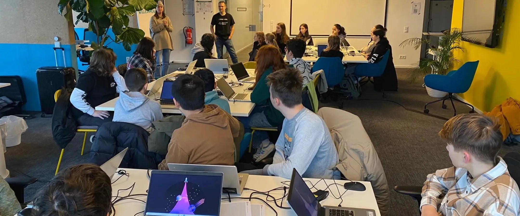 Students from Oranienschule Wiesbaden at the Seibert Group programming days, working on laptops at group tables.