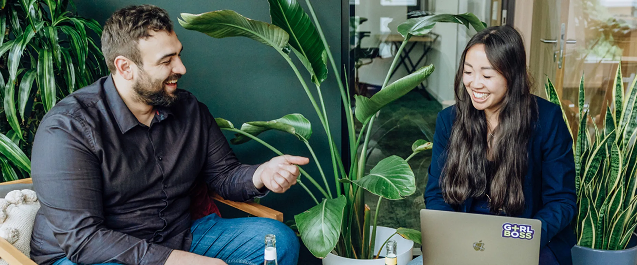 two people smiling and talking with a laptop