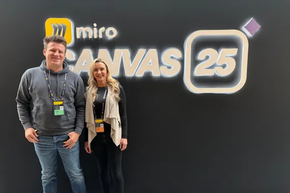 Two colleagues standing in front of the Miro Canvas 25 signage