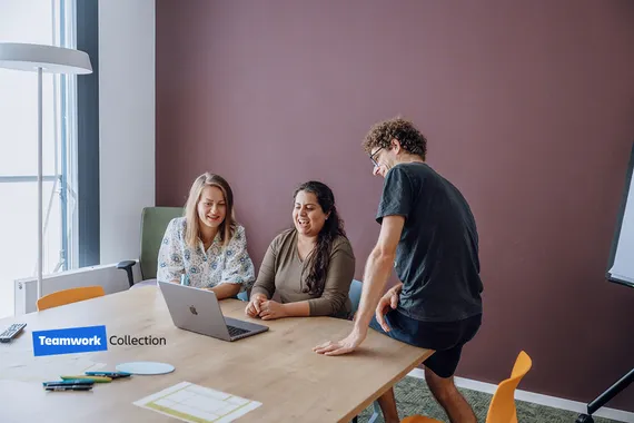 three people sitting at a table looking at a laptop screen