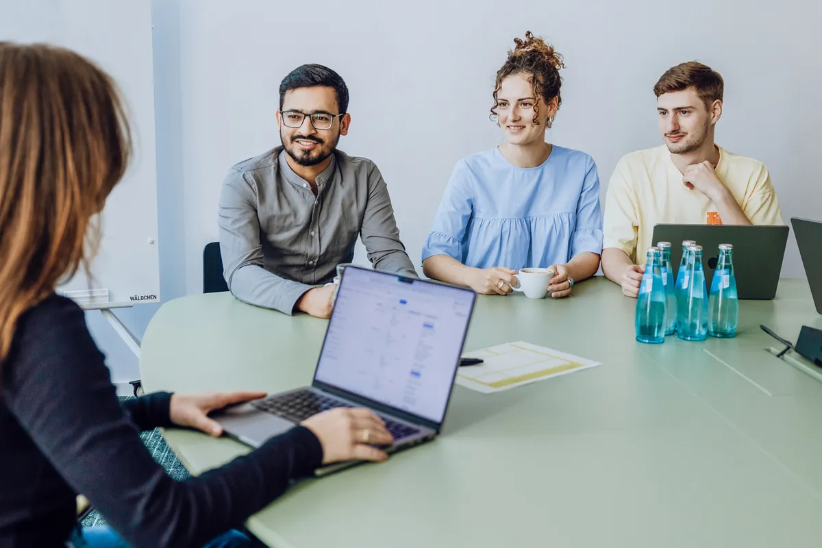 Four people sitting around a table with laptops and water bottles, engaged in a meeting.