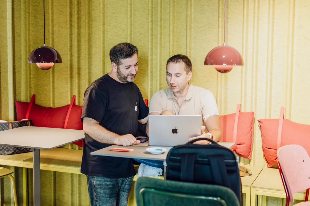 Two men discussing something on a laptop in a modern office setting with colorful decor.