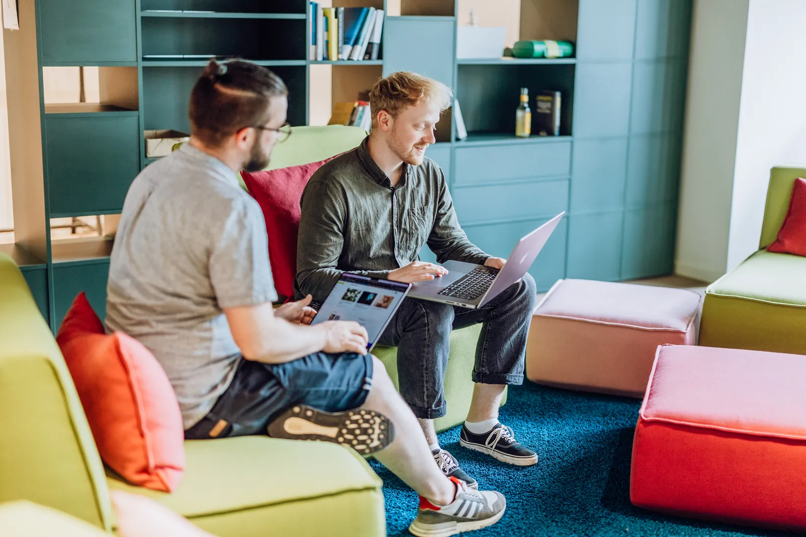 Two men sitting on colorful couches using laptops in a modern office space.