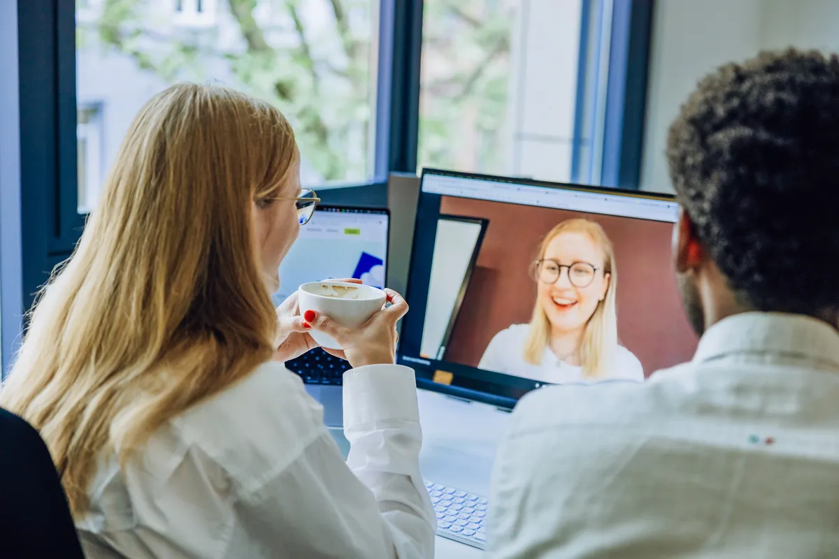 Two people having a video call on a computer screen, with one holding a coffee cup.